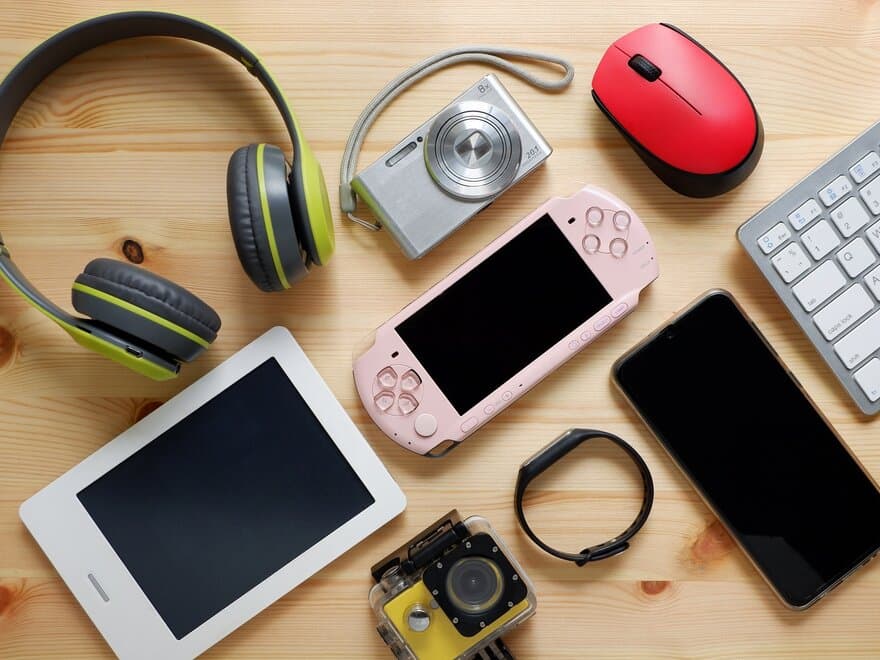 Elektroniske gadgets som smarttelefon, hodetelefoner, kamera, spillkonsoll og tastatur som ligger på et bord. 
